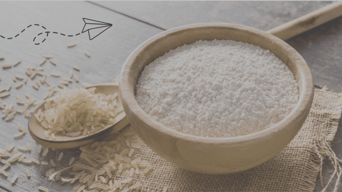 A wooden bowl overflowing with white rice flour next to a wooden spoon holding raw, unpolished rice grains, set on a rustic wooden surface with a burlap accent. The image highlights ingredients for a homemade rice flour face pack, a natural solution for glowing skin.